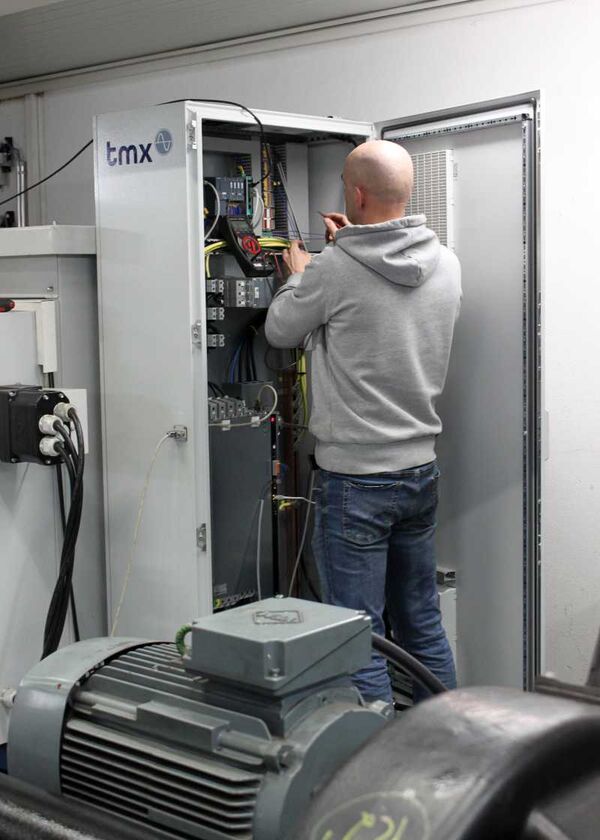 Im Vordergrund ein Elektromotor und im Hintergrund eine Person am einem Schaltschrank