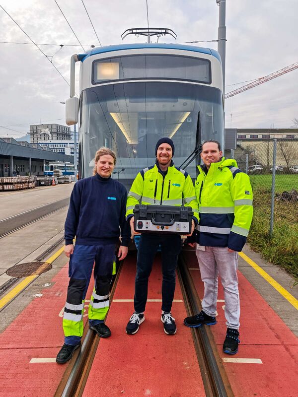 Drei VBZ-Mitarbeiter stehen mit einem schwarzen Hartschalenkoffer mit Anschlüssen vor eine Tram der Verkehrsbetriebe Zürich