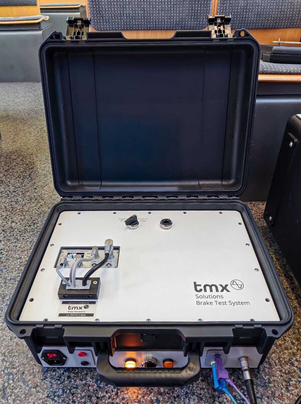 Schwarzer Hartschalenkoffer in einer Tram, der aufgeklappt ist, aber mit einer silbernen Platte mit Schaltern und einem Display verkleidet. An der Stirn des Koffers sind LEDs und Anschlüsse sichtbar.