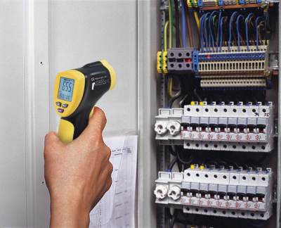 Eine Hand, die ein IR-Pyrometer hält, das auf eine Elektroverteilung gerichtet ist, um die Temperatur zu messen